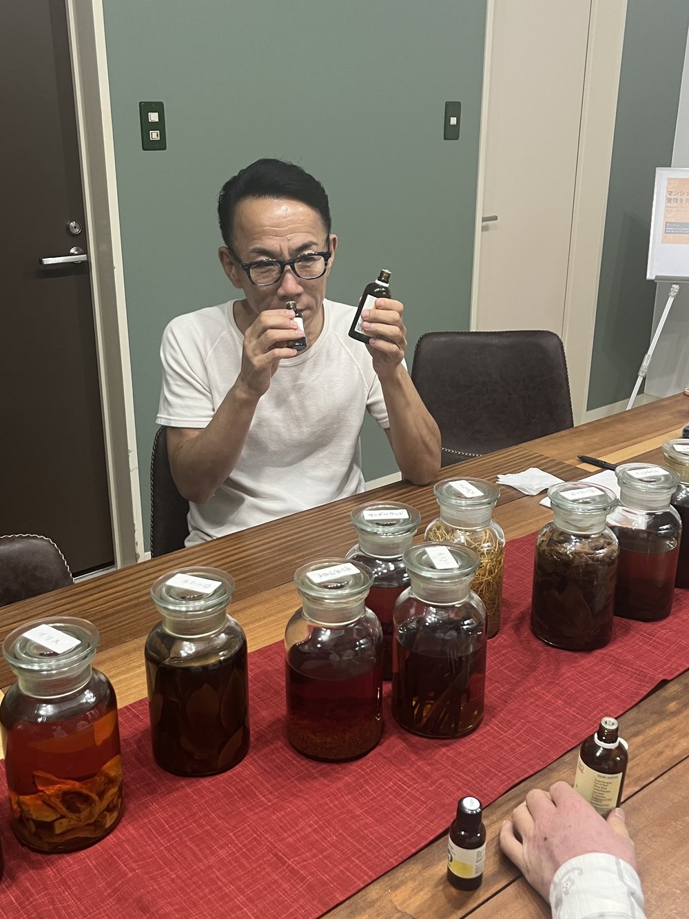 漬け込み瓶の並ぶ机で、小瓶の香りを両手に確かめる長嶋修さん